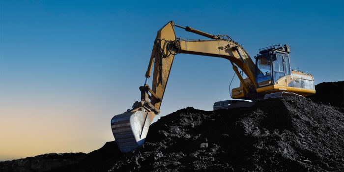 Coal mining in an open pit. Mining excavator loads coal in haul truck in quarry. Excavator digging in open pit coal mine. Excavator in open-pit on sunset background. Heavy machinery in opencast.