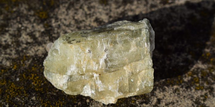 Rough spodumene aka triphane on concrete background, a closeup of transparent yellow green mineral on day light, an outdoor macro shot, geology